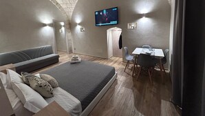 A cozy bedroom with a bed, a seating area, a dining table, and a TV. - The Prince's Mansion (Trani)