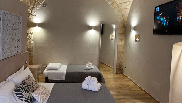 A hotel room with two beds, a TV, and a stone archway. - The Prince's Mansion (Trani)