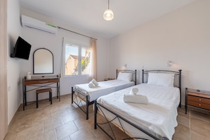 Quarto com duas camas, uma escrivaninha, televisão e janela.