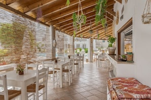 Een restaurant met witte tafels en stoelen, hangplanten en een betegelde vloer.