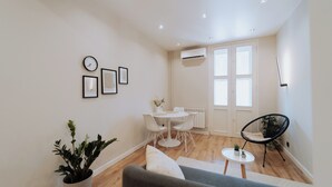 A modern living room with a grey sofa, a small round table, and a black chair. There is a dining table with chairs, a potted plant, and a wall-mounted clock. - Stylish Balcony Apt on Stefan Cel Mare Blvd (Chișinău)