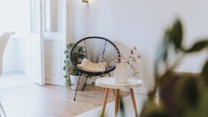 A room with a round wooden table, a white vase with dried branches, a black wicker chair, and a white chair. - Stylish Balcony Apt on Stefan Cel Mare Blvd (Chișinău)