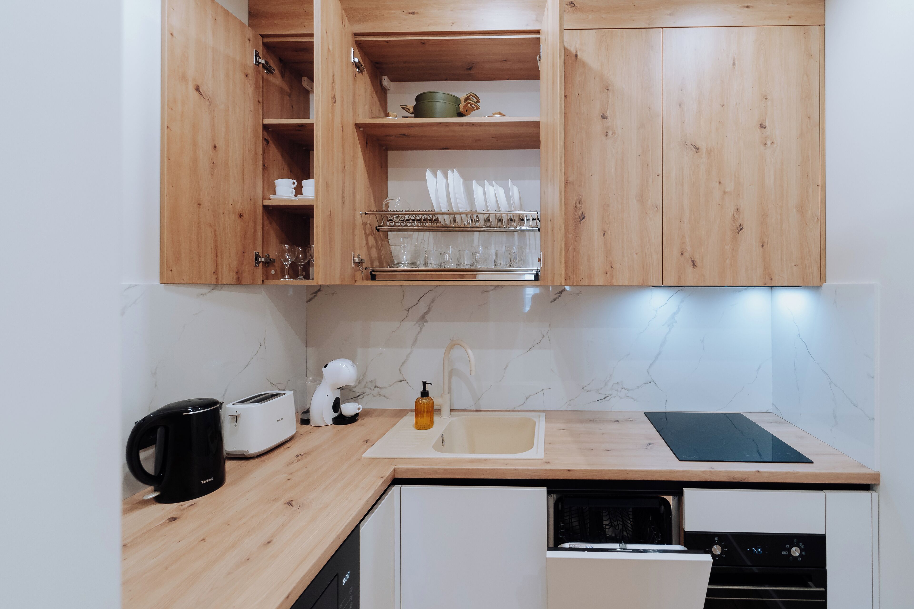 A kitchen with wooden cabinets, a marble backsplash, a sink, a toaster, a kettle, and a dish rack.