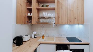 A kitchen with wooden cabinets, a marble backsplash, a sink, a toaster, a kettle, and a dish rack.
