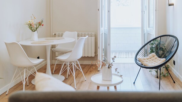 A bright, modern dining area with white furniture, a black wire chair, and a vase of flowers. - Stylish Balcony Apt on Stefan Cel Mare Blvd (Chișinău)