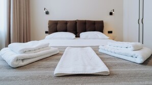 A neatly made bed with white linens and a brown headboard. There are folded towels on the bed and a flat white towel in front. - Stylish Balcony Apt on Stefan Cel Mare Blvd (Chișinău)