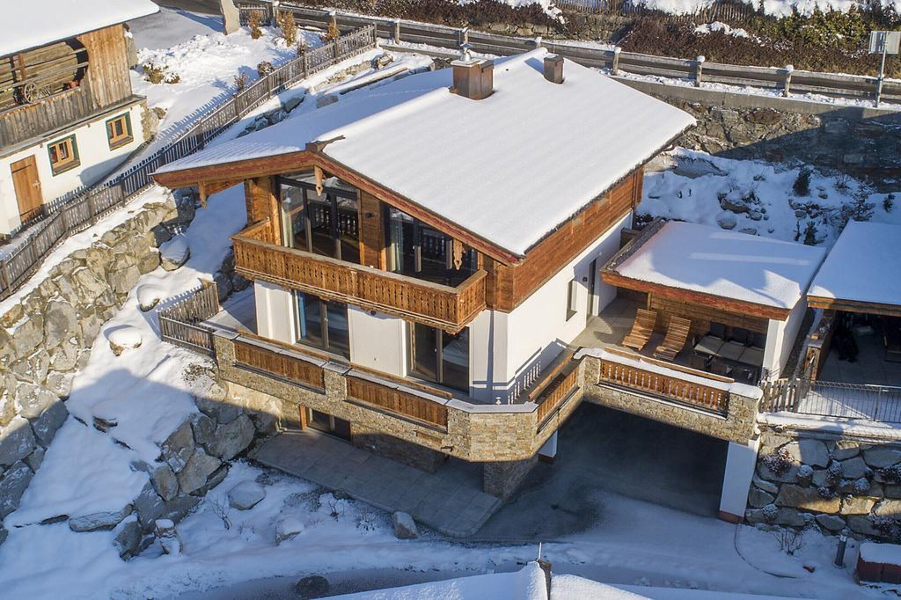 A two-story chalet with a snow-covered roof, wooden balconies, and stone walls.