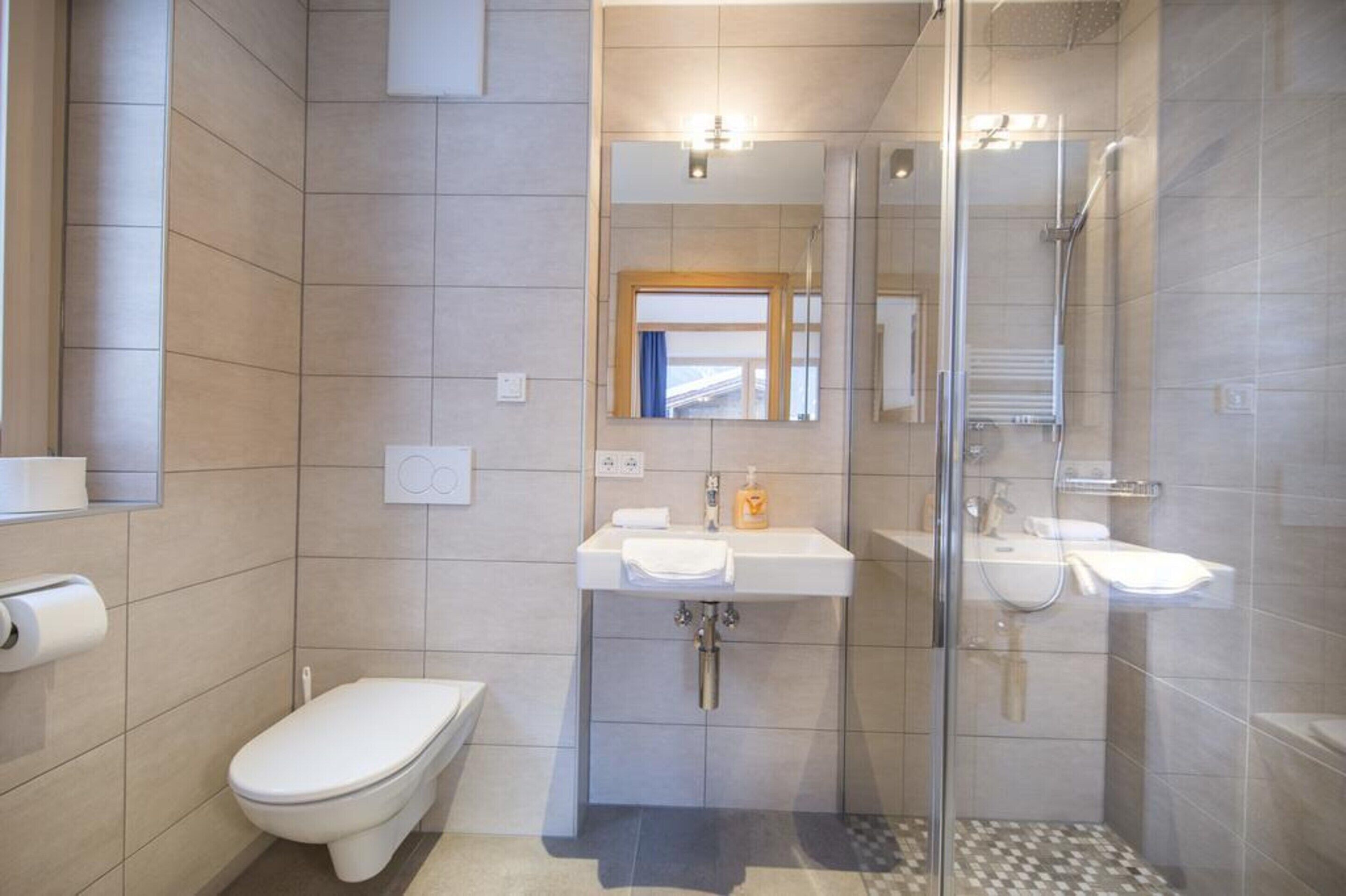 Un baño moderno con inodoro, dos lavamanos, ducha y zona de ducha con mampara de vidrio.
