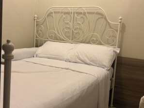 Un cadre de lit en métal blanc, agrémenté d’une tête de lit décorative, un lit bien fait avec du linge de lit blanc et un plancher en bois.