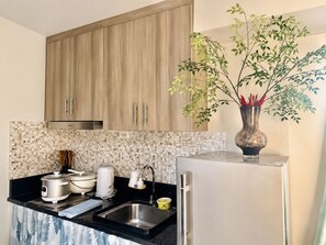 A kitchen with wooden cabinets, a tiled backsplash, a stainless steel sink, a refrigerator, and a potted plant.