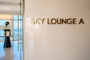 Letrero que indica 'SKY LOUNGE A' en un interior moderno con vista a través de un ventanal.