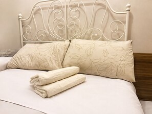 A bed with a white metal headboard, two pillows with a leaf pattern, and two folded towels.