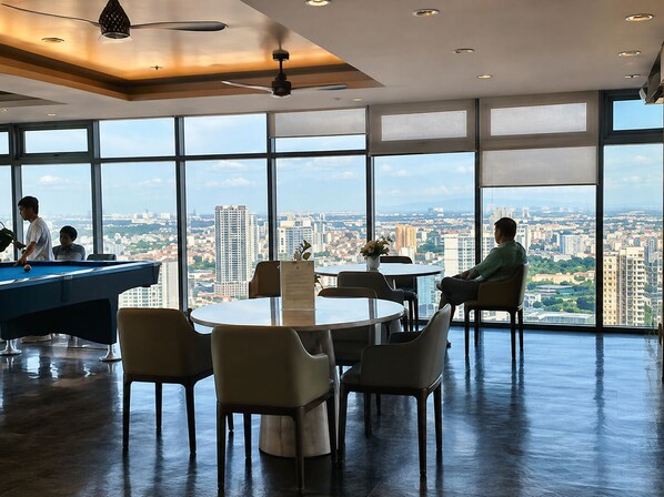 A spacious room with a pool table, comfortable seating, and large windows offering a city view.