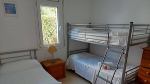 Et soveværelse med køjesenge, et natbord med lampe, en kommode og et vindue med udsigt til grønne områder.