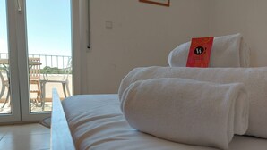 Et hotelværelse med en seng, to hvide håndklæder og en balkon med havemøbler.