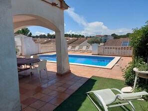 A rooftop pool area with a table and chairs, surrounded by a white wall and a green lawn.