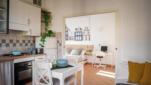 A compact kitchen with a dining area, a bed, and a view of buildings. - Accomodo MIM21 Monolocale Porta Venezia (Milan)