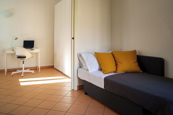 A bedroom with a bed, a desk with a laptop, and a chair.