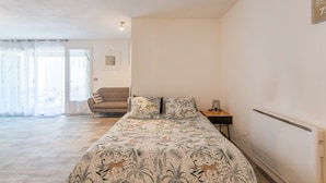 A bedroom with a bed, a nightstand, a sofa, and a view of the outside.