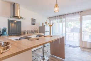 A modern kitchen with a central island, stainless steel range hood, and a pendant light. - Apartment “At the Foot of Sainte Victoire” with Private Terrace, Garden & Wi-Fi (Puyloubier)