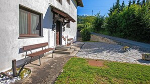 Ein weißes Gebäude mit einem steinernen Weg, der zu einer hölzernen Bank und einer Treppe führt.