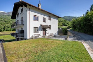 Une maison à deux étages avec un balcon, une porte d’entrée et un petit porche doté de bancs.