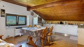 Ein Essbereich mit Tisch und Stühlen, ein Fenster mit Blick, eine Küche mit Schränken und Geräten sowie eine Holzbalkendecke.