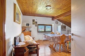 Une pièce chaleureuse avec un plafond en bois, une table à manger avec des chaises, une petite kitchenette et une fenêtre donnant sur un beau paysage.