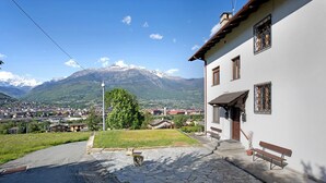 Ein Gebäude mit einem gepflasterten Innenhof, einer Bank und Blick auf die Berge.
