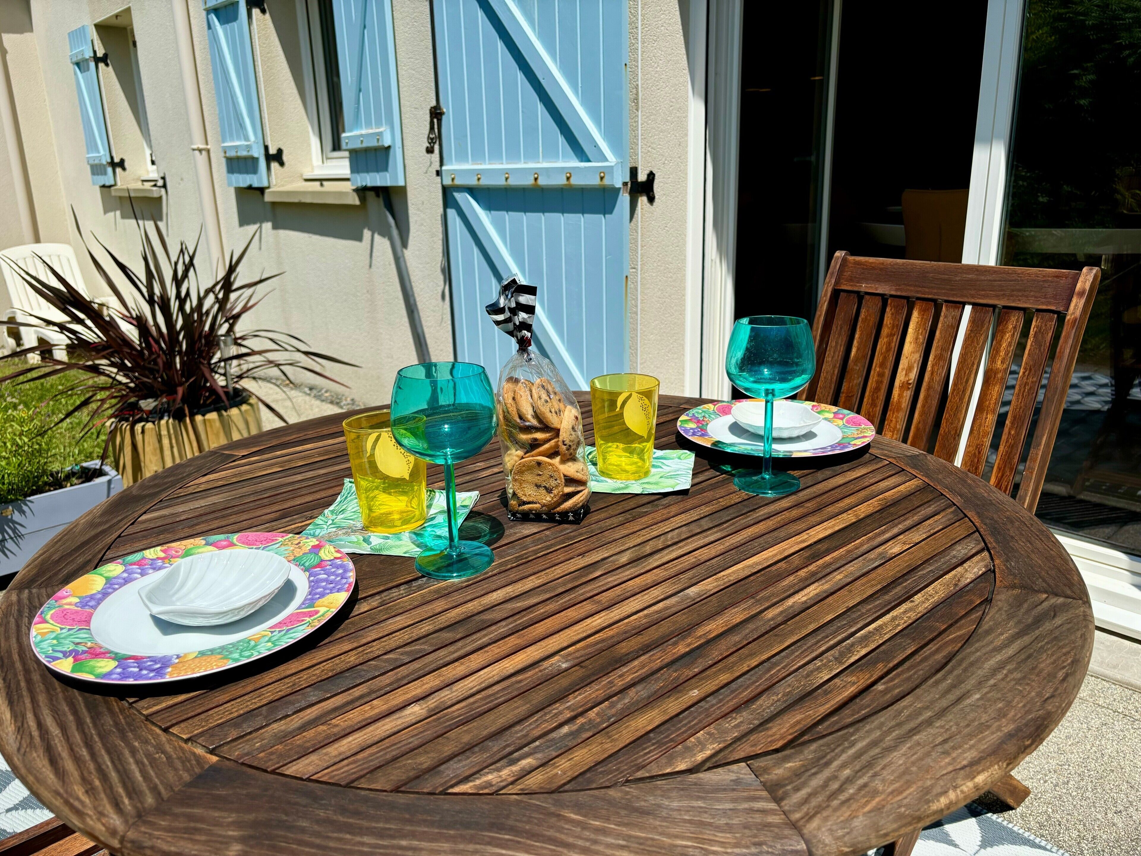 Une table ronde en bois, sur laquelle se trouvent une assiette décorée de motifs floraux, deux verres et un sachet de biscuits.