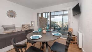 A modern room with a dining table, chairs, a sofa, a TV, and a large window.