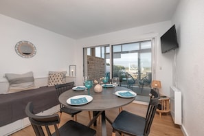 Une pièce moderne comprenant une table à manger, des chaises, un canapé, un téléviseur et une grande fenêtre.