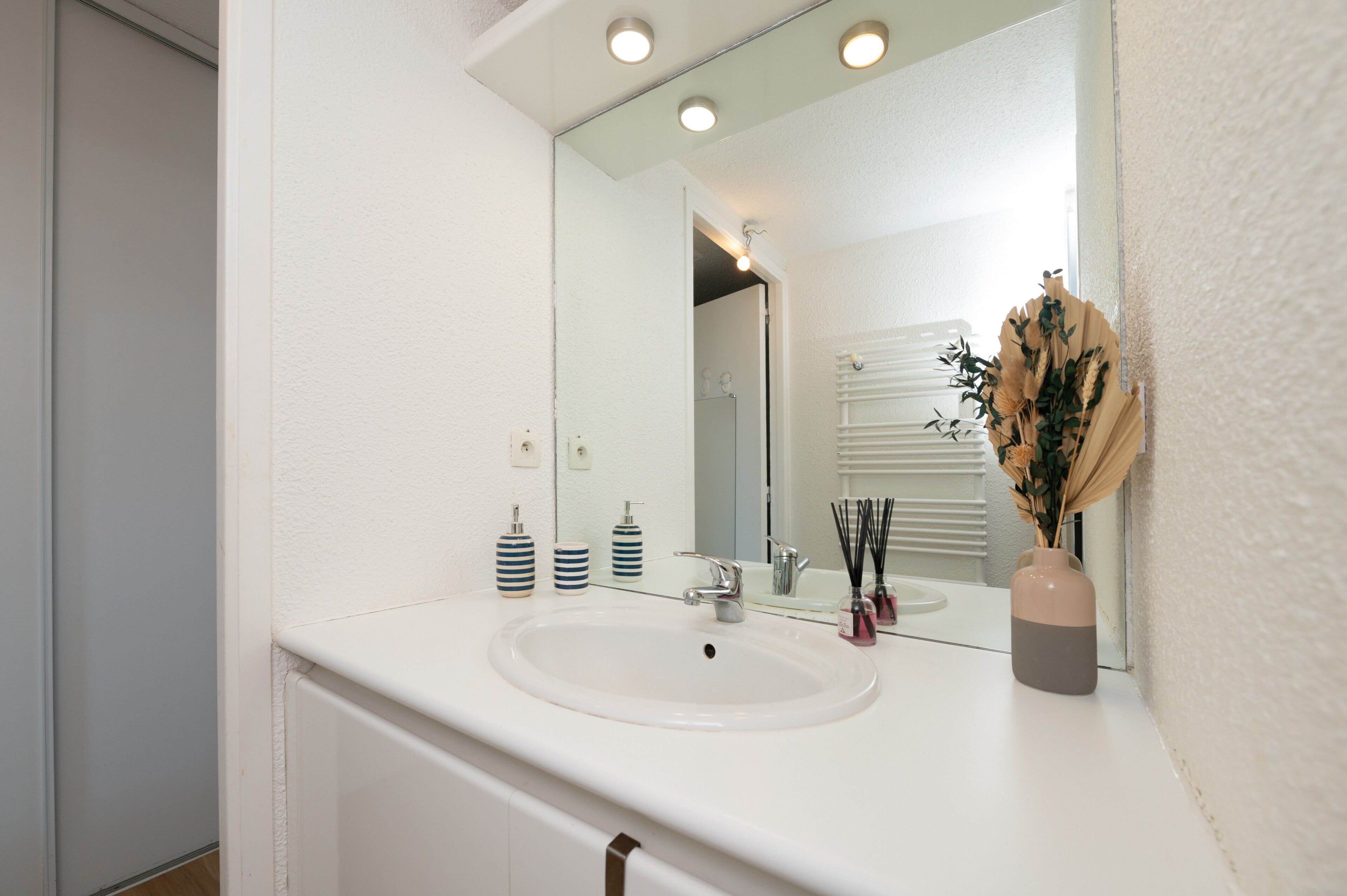 A bathroom with a white sink, mirror, and a vase with dried flowers.