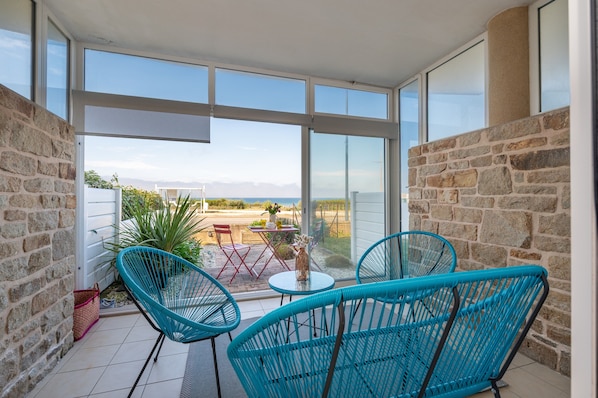 A balcony with a view of the sea, stone walls, and blue chairs.