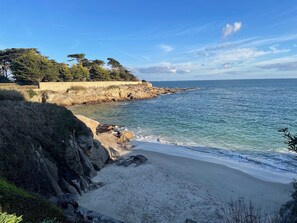 A coastal landscape with a sandy beach, rocky cliffs, and a clear blue sky.