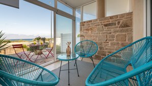 A balcony with a glass table and chairs, a stone wall, and a view of the landscape.
