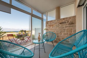Un balcon avec une table et des chaises en verre, un mur en pierre et une vue sur le paysage.