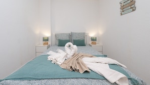 A neatly made bed with a teal bedspread, two pillows, and a towel arrangement. There are two bedside tables with lamps and a wall-mounted sign.