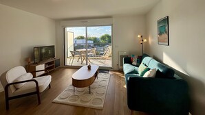 A living room with a sofa, a coffee table, a TV, and a balcony with a view.