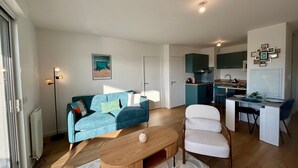 A modern living room with a sofa, a coffee table, and a dining area with a kitchen in the background.