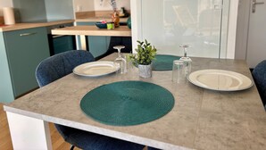 A dining table with placemats, plates, and glassware in a modern kitchen with teal cabinets and a view through a glass door.