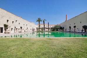 A courtyard with a pool, palm trees, and a building with a red chimney.