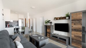 A modern living room with a grey sofa, a coffee table, and a flat-screen TV mounted on a wooden wall. - Vacation 'Gabriela' with Shared Pool, Balcony and Wi-Fi (Candelaria)