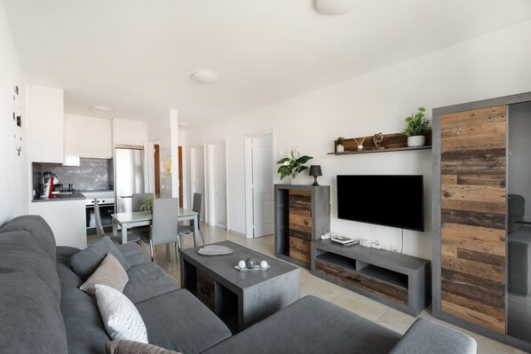 A modern living room with a grey sofa, a coffee table, and a flat-screen TV mounted on a wooden wall.