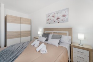 A neatly made bed with pillows and a blanket, a bedside table with a lamp, and a wall-mounted painting of flowers.