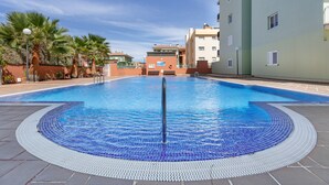 A swimming pool with a tiled edge, surrounded by palm trees and buildings. - Vacation 'Gabriela' with Shared Pool, Balcony and Wi-Fi (Candelaria)