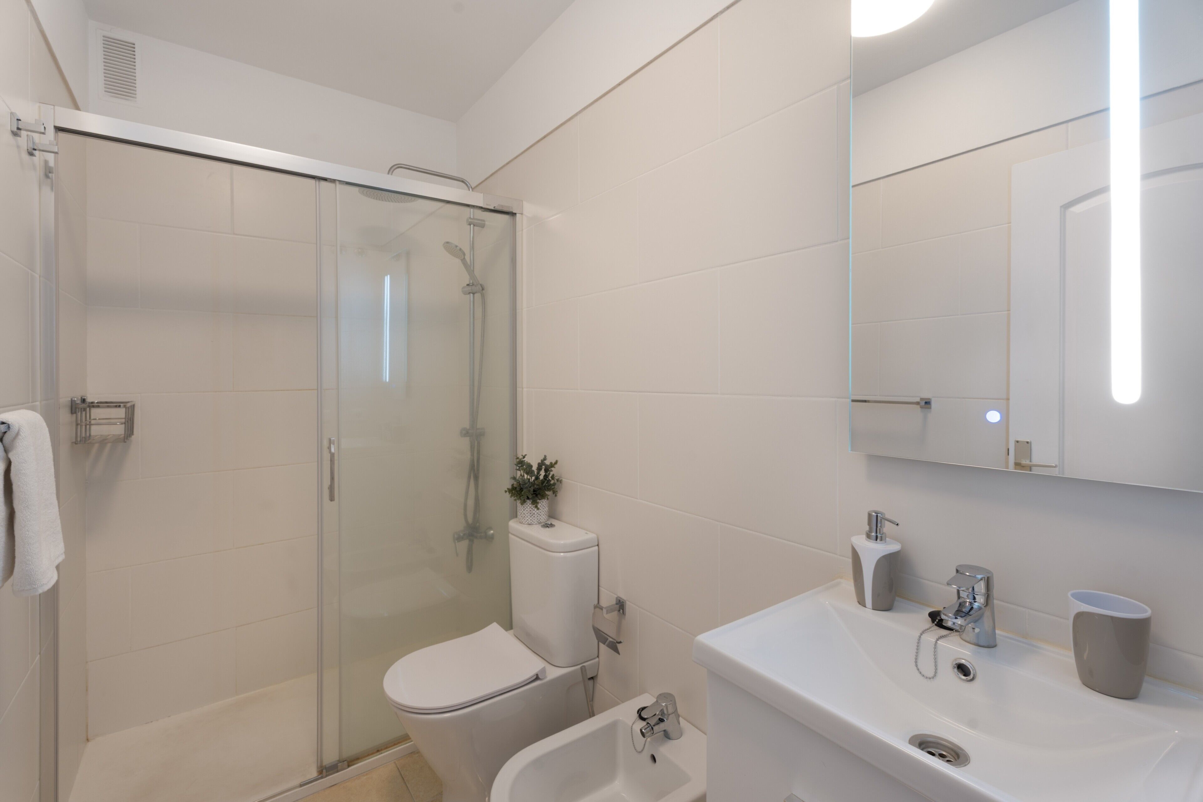 Un baño moderno con cabina de ducha de vidrio, inodoro, bidé y lavamanos con espejo.