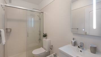 Un baño moderno con cabina de ducha de vidrio, inodoro, bidé y lavamanos con espejo.