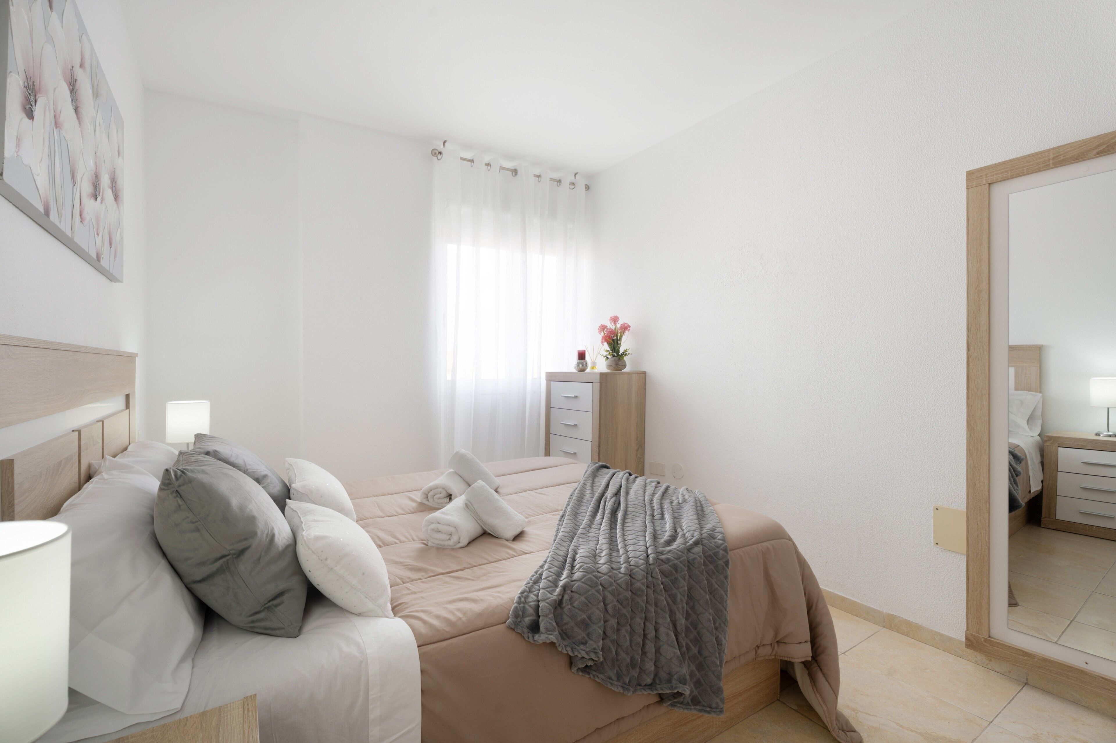 A bedroom with a bed, bedside table, lamp, and a mirror.