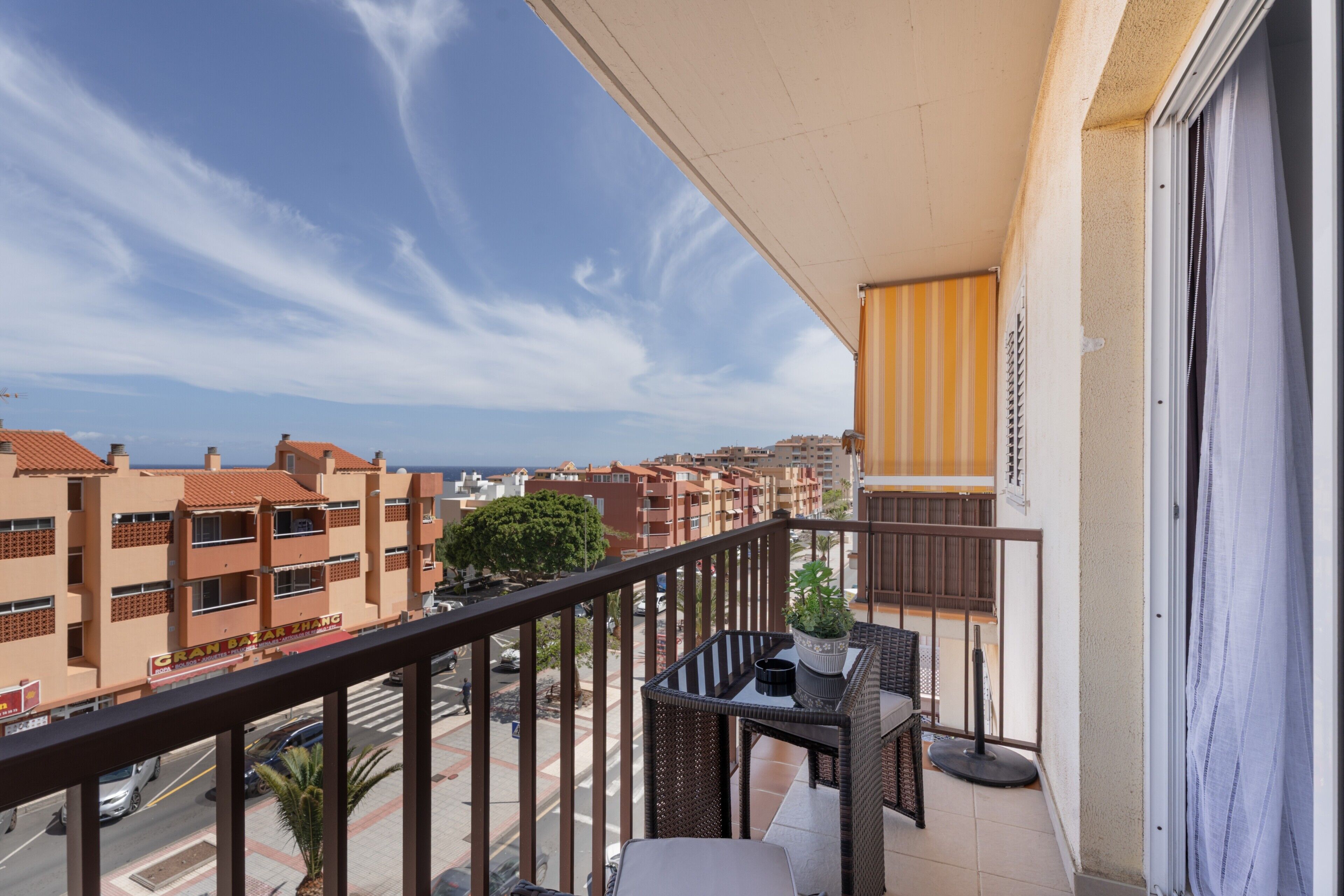 A balcony with a view of buildings, a table with chairs, and a potted plant.